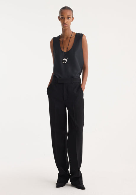 A slender person wears Straight leg trousers | black, showcasing high-waisted tailoring, sharp pleats, and side pockets, paired with a minimalist black scoop-neck top.