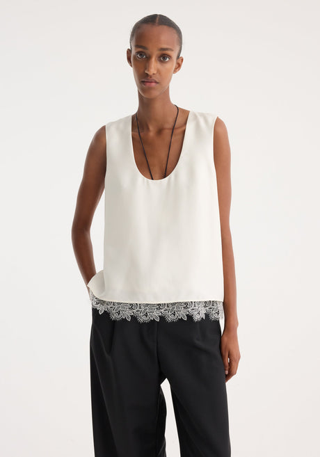 Model wearing a cream lace-trimmed silk top with a deep scoop neckline, paired with wide-leg black trousers, showcasing minimalist style and intricate lace detailing.