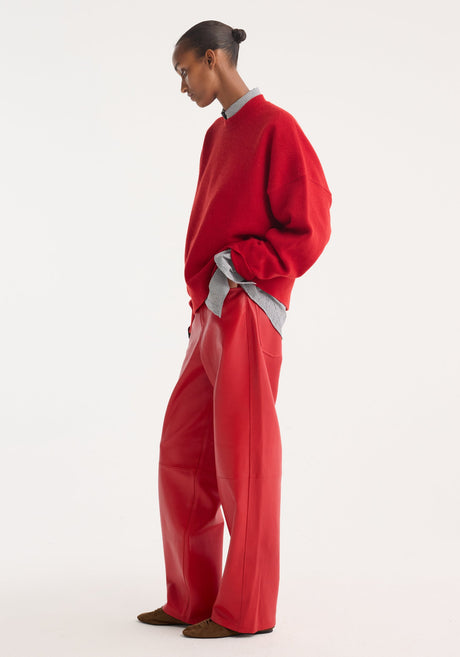 Model wearing Baggy Leather Trousers | Rosso, featuring a high-waist, wide-leg fit in soft nappa lamb leather, paired with a red sweater and loafers.