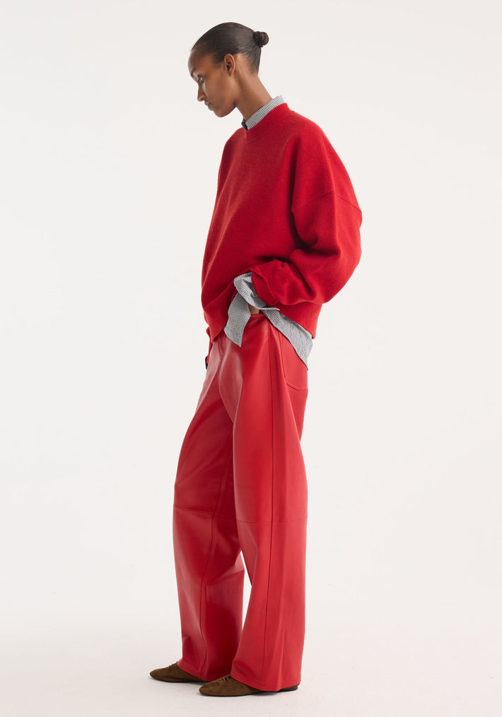 Model in profile wears Baggy leather trousers | rosso, high-waisted with a wide-leg fit, paired with an oversized sweater and grey shirt; shoes are brown slip-ons.