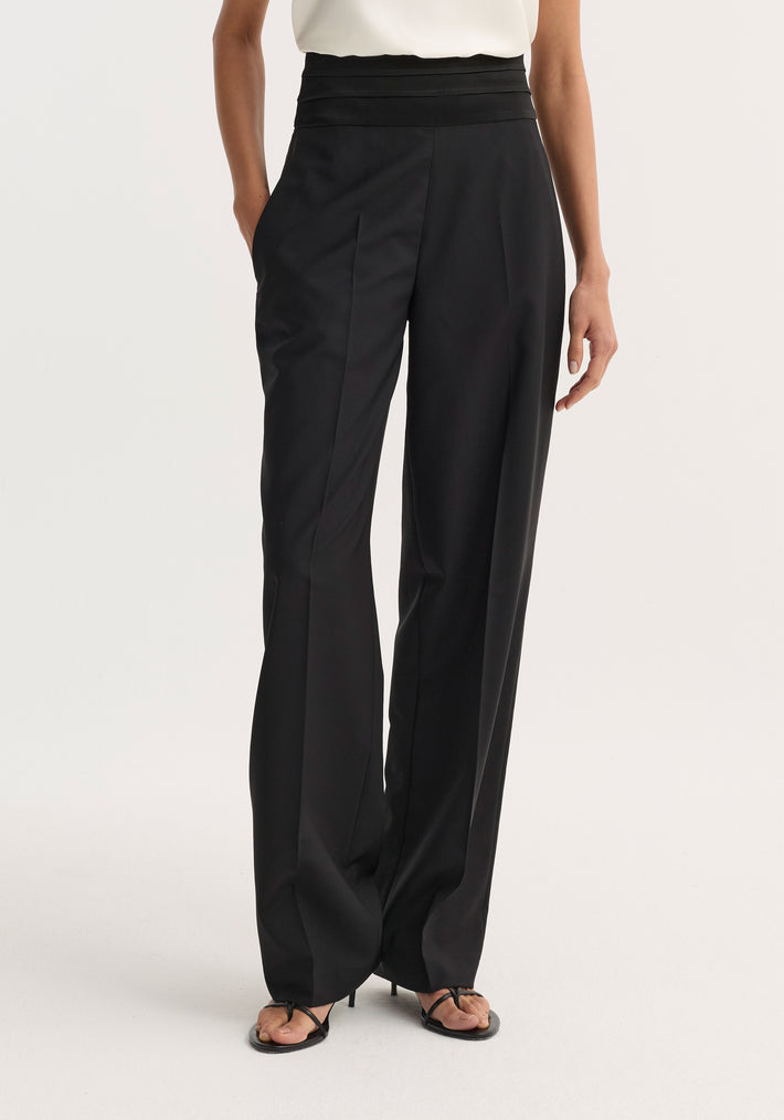 Satin cumberband trousers in black, featuring a high-waisted, wide-leg design with front pleats, side pockets, and strappy heeled sandals.