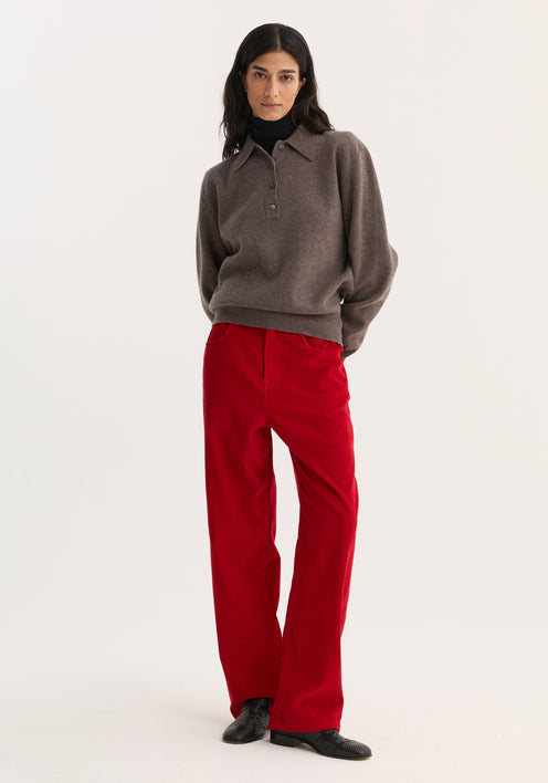 Woman wearing Relaxed Corduroy Trousers in Rosso, paired with a knit polo sweater and black shoes, showcasing the pants' vibrant hue and denim-inspired details.