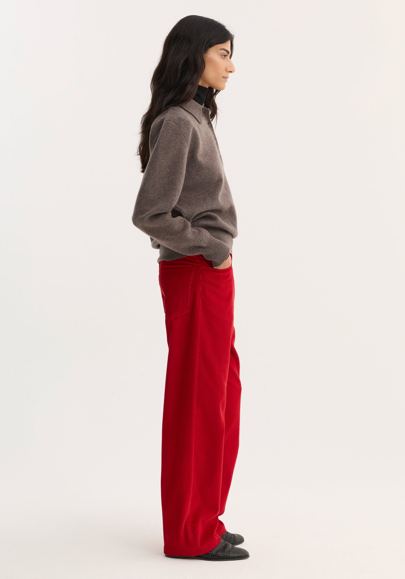 Side-profile of a model wearing Relaxed corduroy trousers | rosso, showcasing vibrant red, wide-leg corduroy pants with denim-style details, paired with a brown sweater.