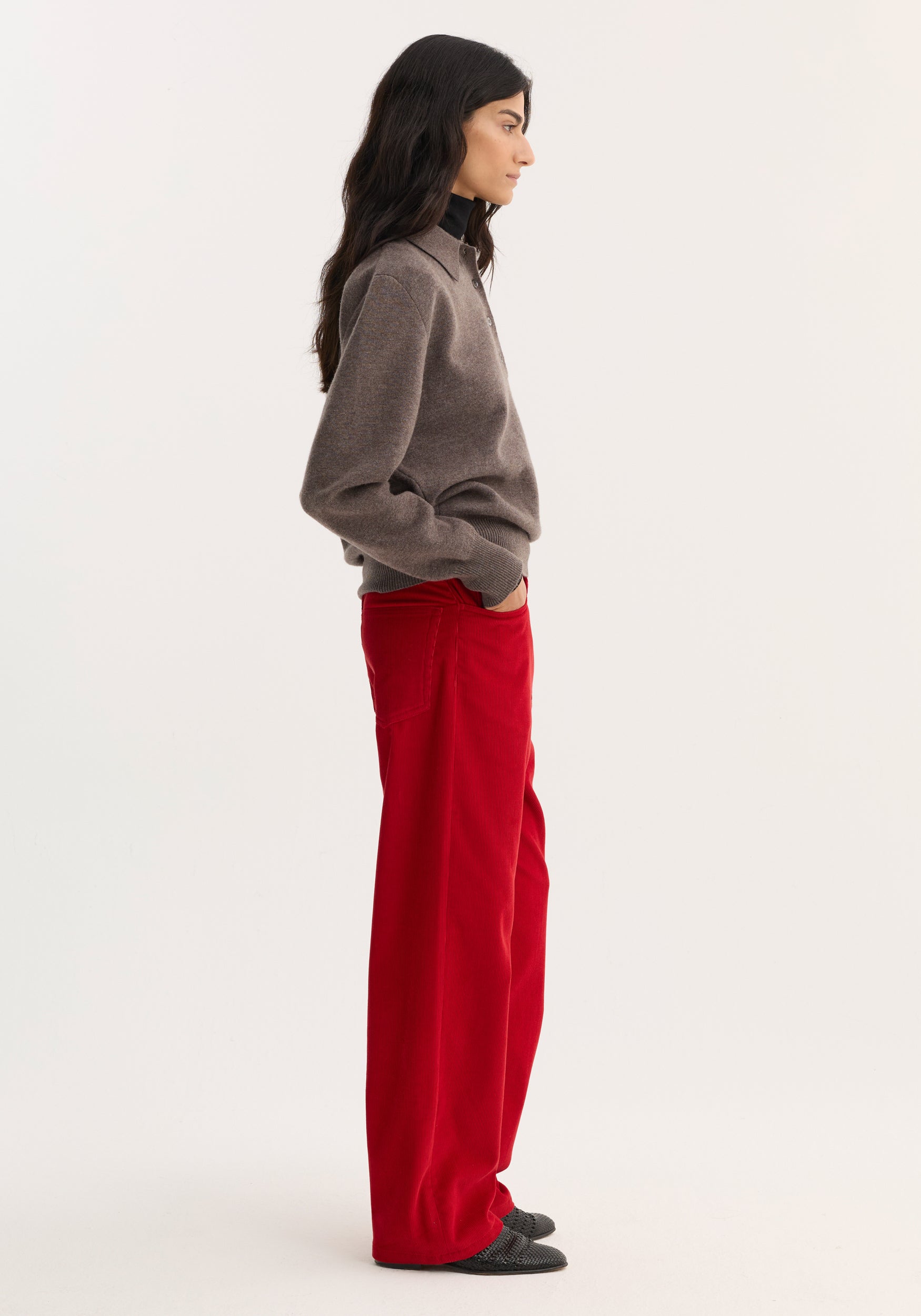 Side-profile of a model wearing Relaxed corduroy trousers | rosso, showcasing vibrant red, wide-leg corduroy pants with denim-style details, paired with a brown sweater.