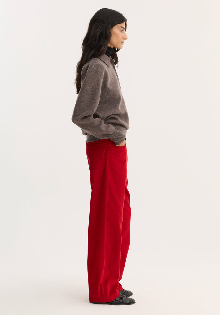 Woman wearing Relaxed Corduroy Trousers in Rosso, paired with a knit polo sweater and black shoes, showcasing the pants' vibrant hue and denim-inspired details.