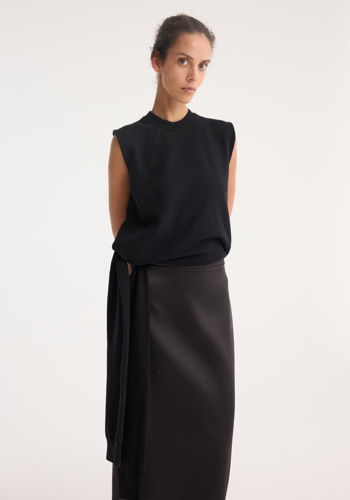 Slim woman models the Open-back sash wrap top, featuring deconstructed sleeves, open back, and wrap waist, paired with a high-waisted black skirt.