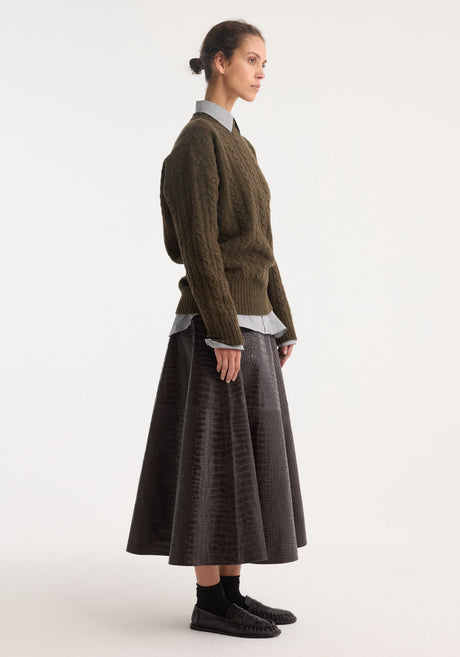 Model wearing the A-line croco skirt in mahogany, featuring a glossy, embossed finish, paired with a green knit sweater and loafers.