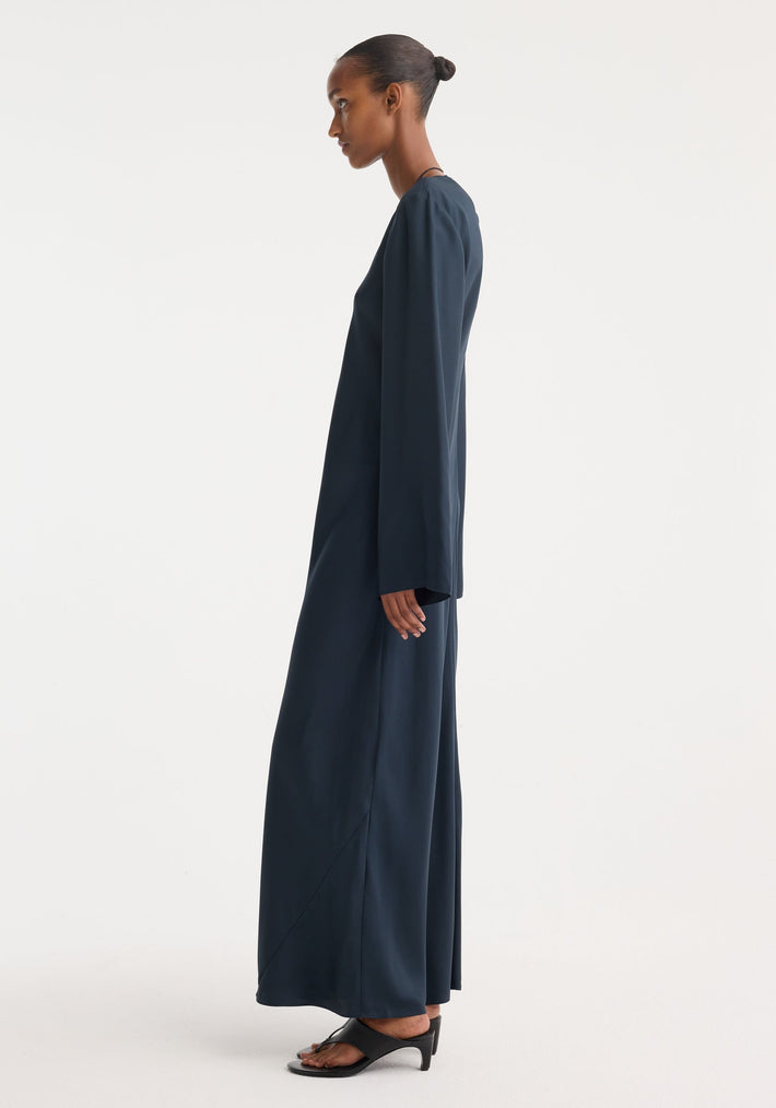 Model in a Signature silk dress | storm, featuring a minimalist, floor-length design with wide sleeves and a soft drape, paired with black sandals.