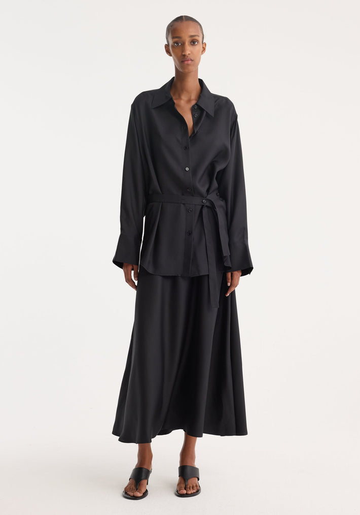 Silk gilet-dress in black, features a deconstructed design with open armholes and a wrap belt, worn by a tall woman for a minimalist look.