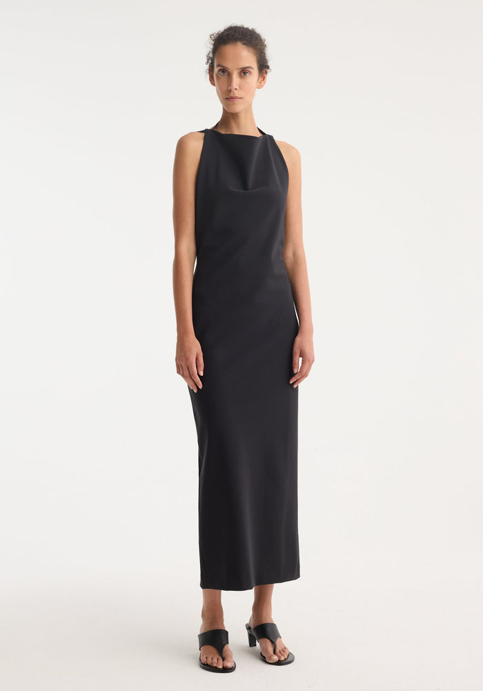 Model in Open Back Dress | Black, featuring a high halter neckline, tie detail, column silhouette, full open back, and back slit.