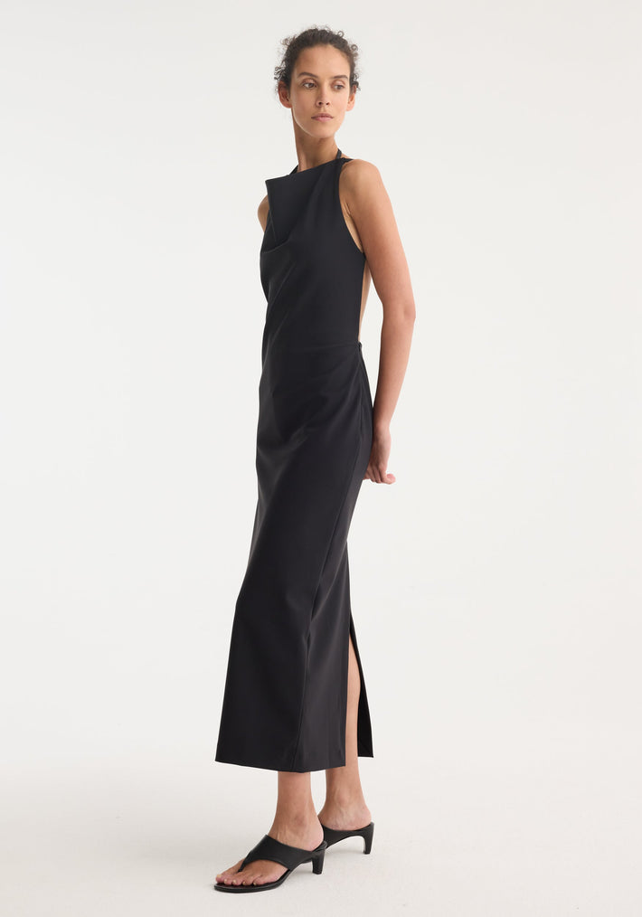 Model in profile wearing Open back dress | black, featuring a high halter neckline, tie detailing, floor-length silhouette, side slit, and open back with heeled mule sandals.