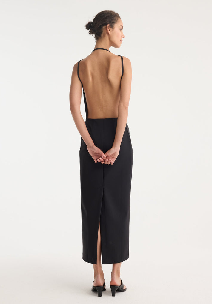 Open back dress | black, featuring a high halter neckline, slim fit, full open back, and mid-calf length with a center-back slit. Model's hair in a loose bun.