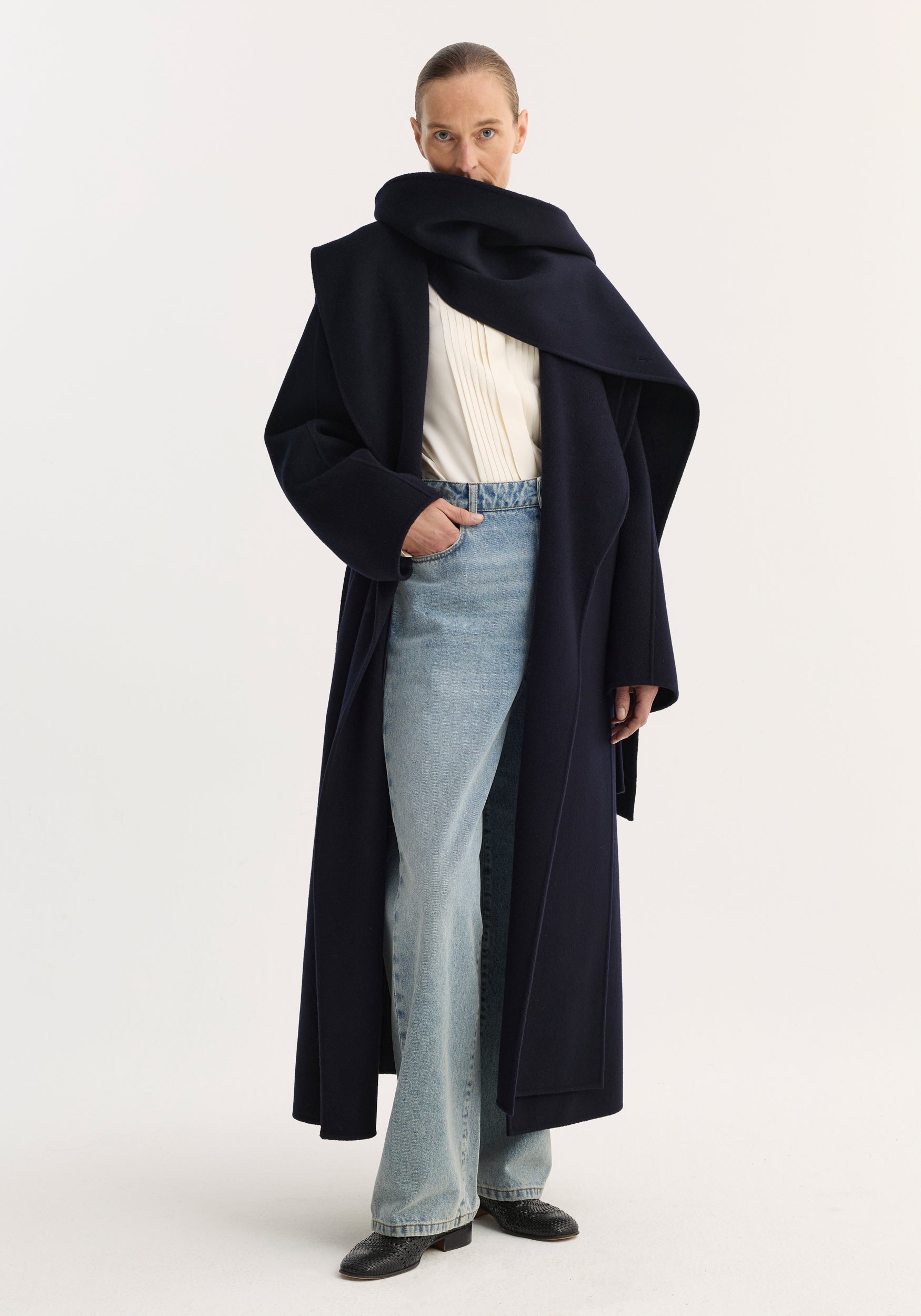 Woman wearing a navy Signature double-faced scarf coat layered over a white blouse and light blue jeans, standing against a plain white background.