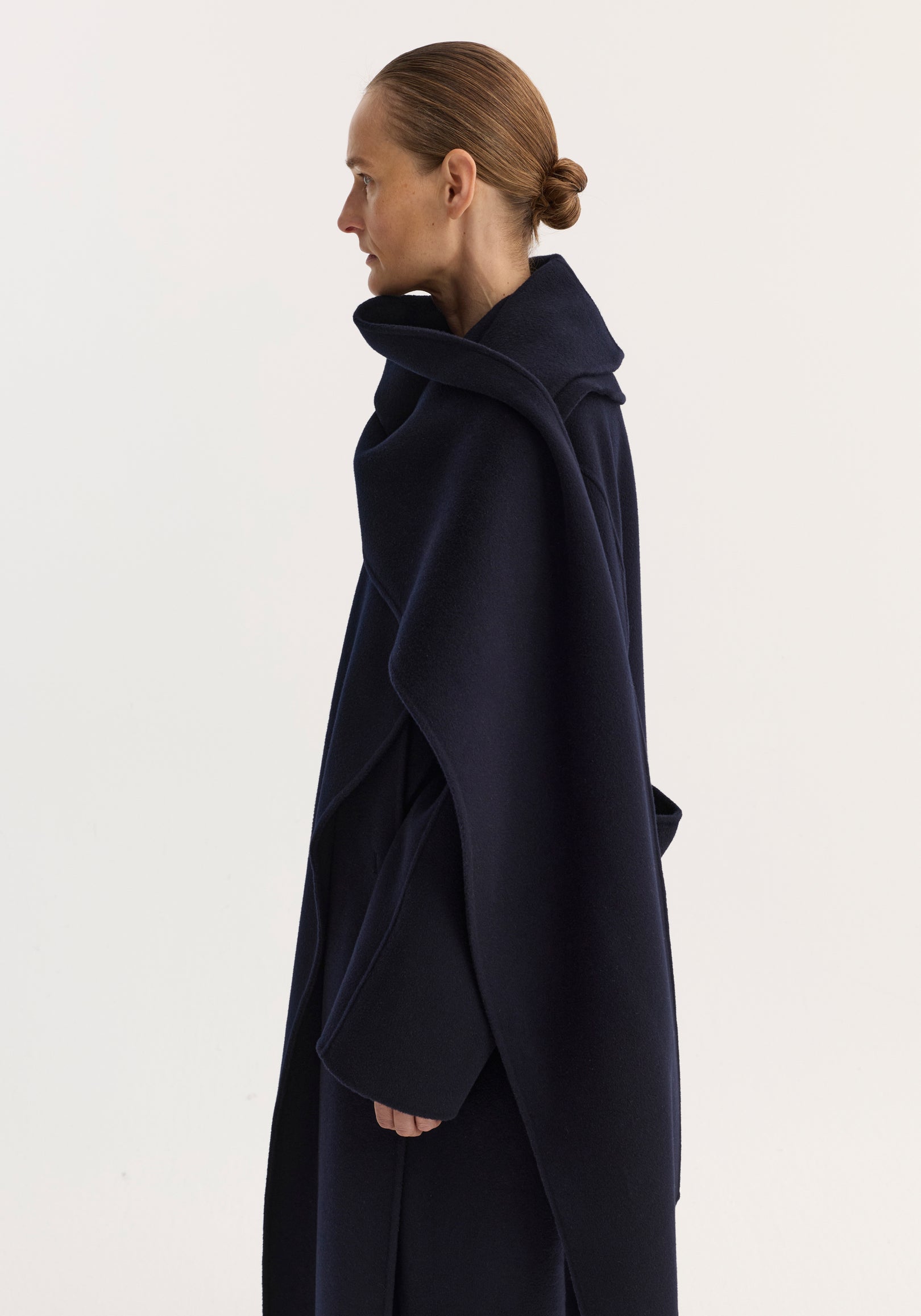 Woman in profile wearing a navy Signature double-faced scarf coat with draped collar and long sleeves against a plain light background.