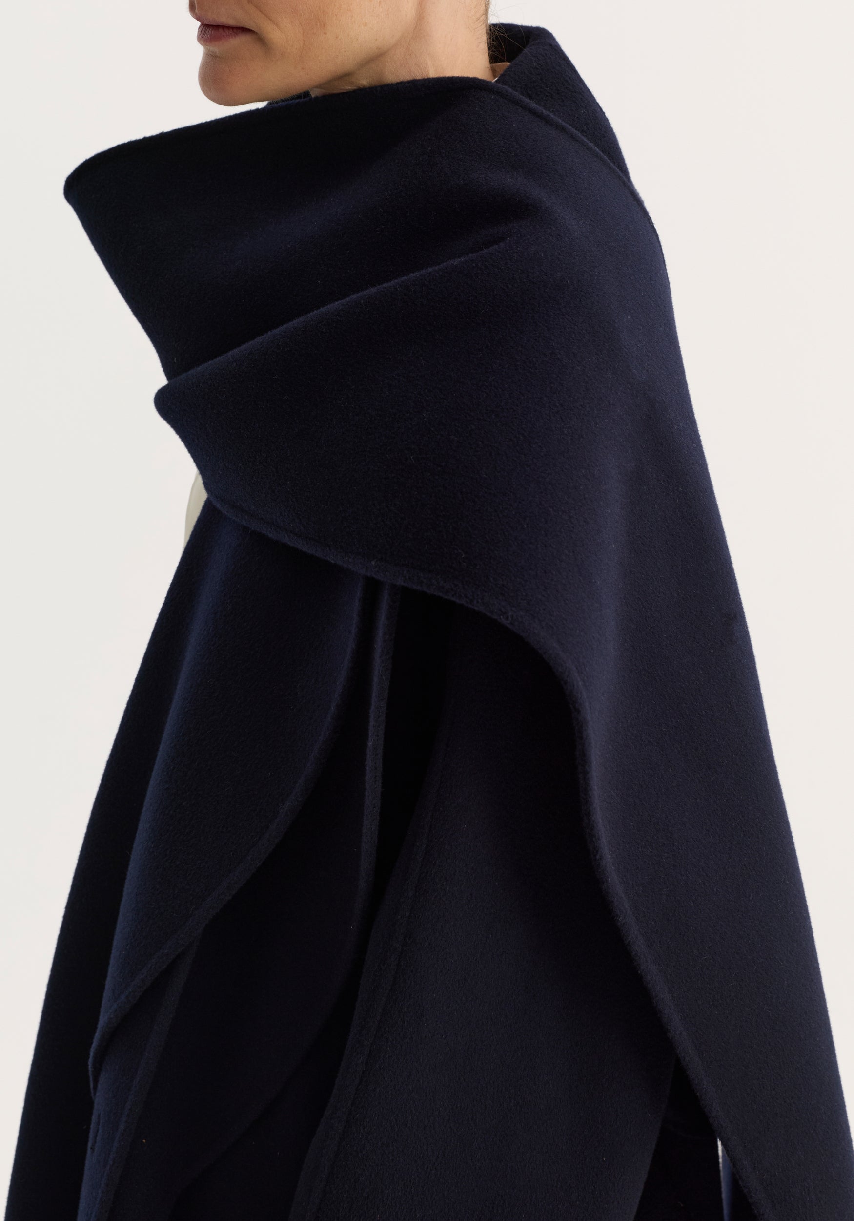 Close-up of a person wearing the Signature double-faced scarf coat | navy, showcasing its soft texture and deep navy color with a layered, draped design around the shoulders.
