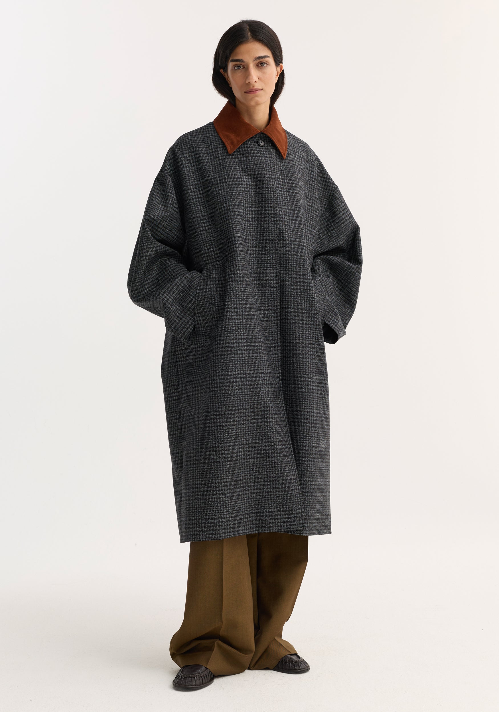 Woman wearing a long black and grey check coat with a contrasting brown suede collar, styled with wide-leg brown pants and black shoes, standing against a plain background, featuring the Suede collar check coat | black / grey check.