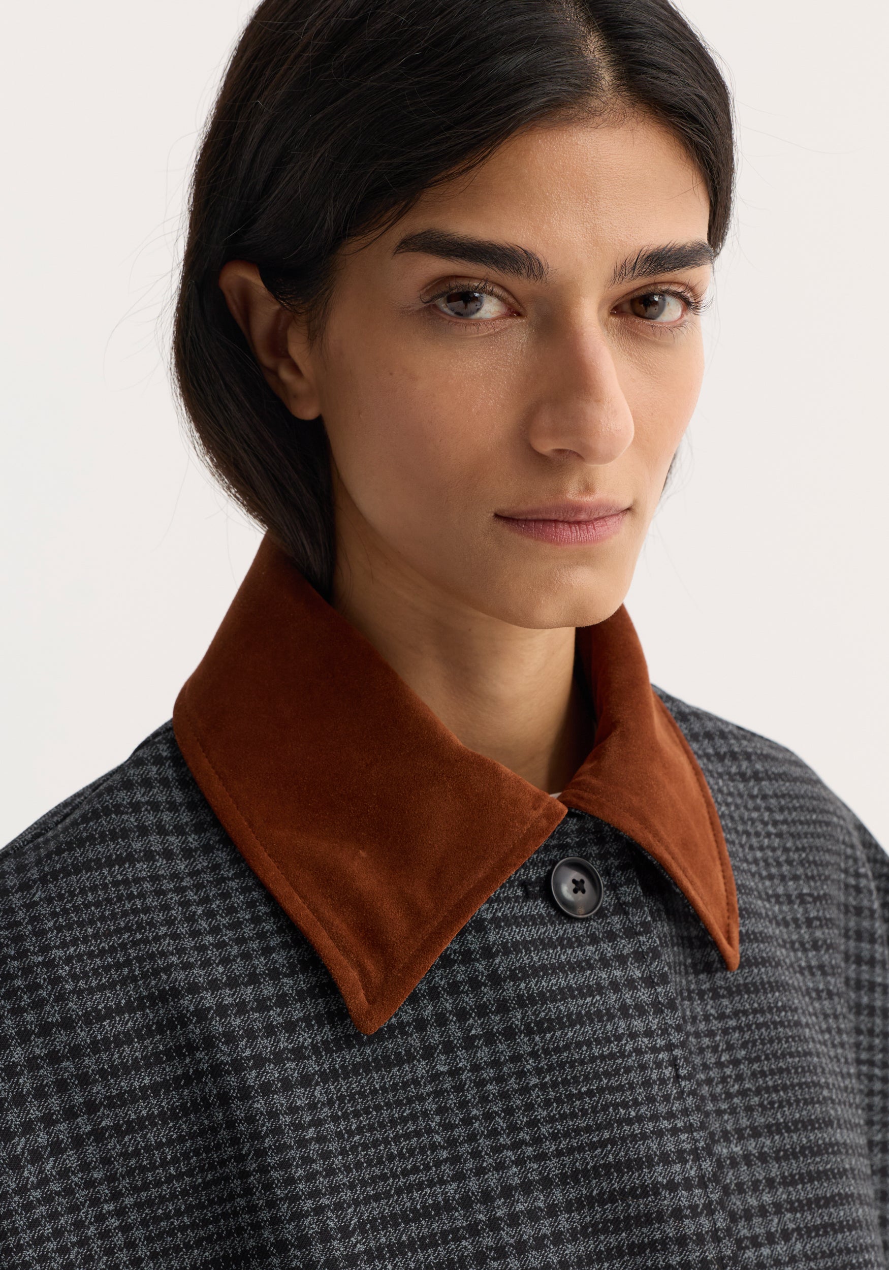 Close-up of a woman wearing a Suede collar check coat | black / grey check featuring a brown suede collar and black and grey check pattern fabric.