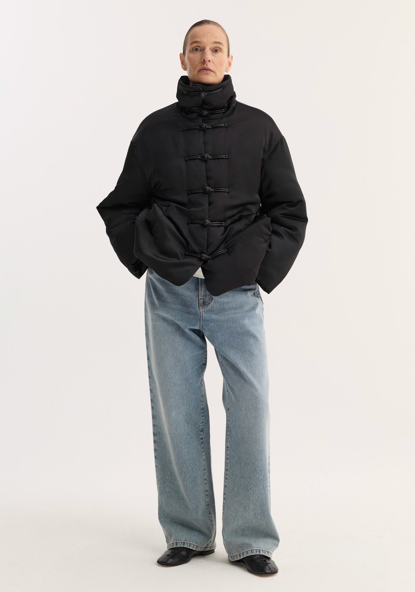 Model wearing Padded Puffer Jacket | Black with high quilted collar, pankou closures, and slanted welt pockets, paired with light-wash jeans and black shoes.