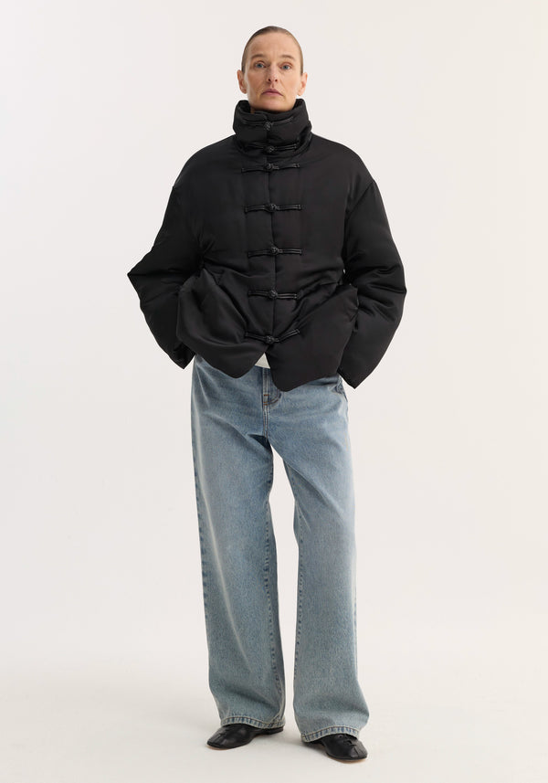 Model wearing Padded Puffer Jacket | Black with high quilted collar, pankou closures, and slanted welt pockets, paired with light-wash jeans and black shoes.