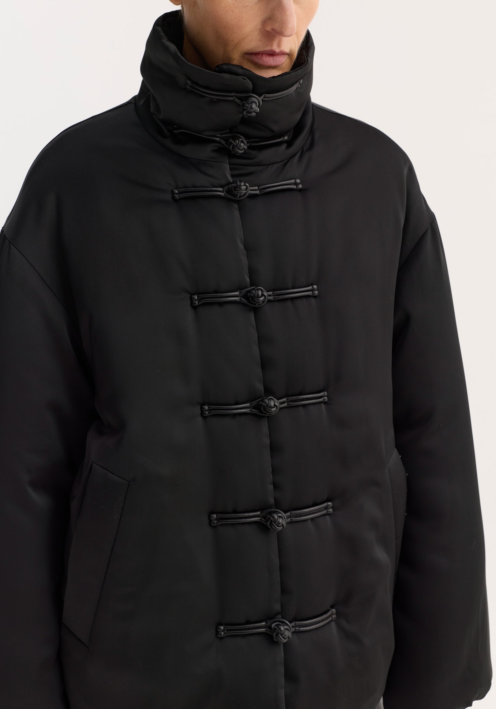 Close-up of a person wearing a black padded puffer jacket | black with a high collar and toggle button closures down the front.