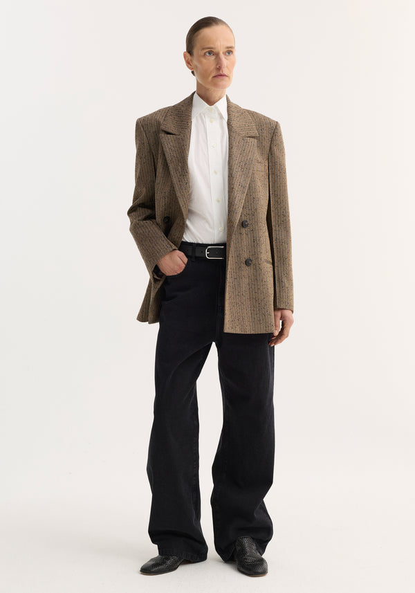 Person wearing a double-breasted blazer with herringbone texture, featuring broad lapels, chest and welt pockets, paired with a white shirt and black trousers.
