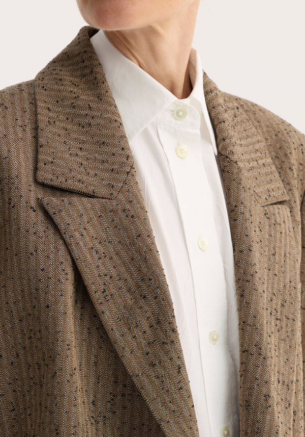 Double-breasted blazer with a herringbone weave, showcasing a sharp shoulder line, visible buttons, and a white shirt collar underneath.