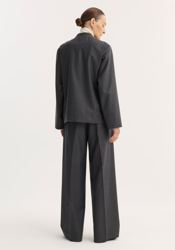 Person wearing a Pankou closure jacket in dark grey melange, featuring patch pockets, over a light turtleneck. Model's hair is styled in a low bun.