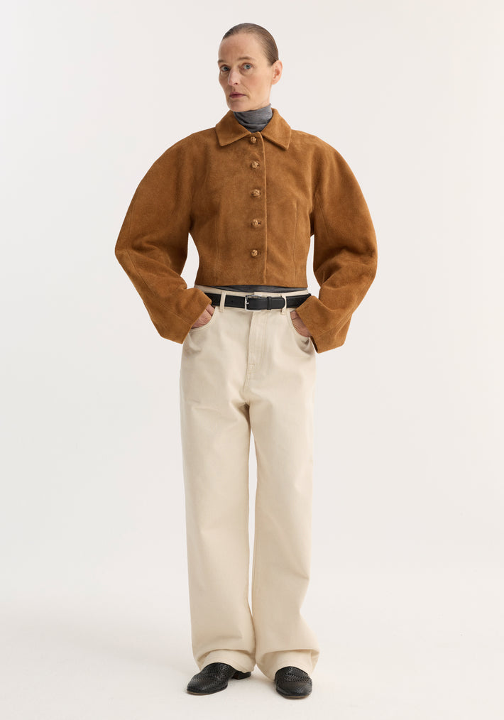 Woman wearing a Rounded textured suede jacket | cognac over a gray turtleneck, paired with high-waisted cream trousers and black loafers, hands in pockets.