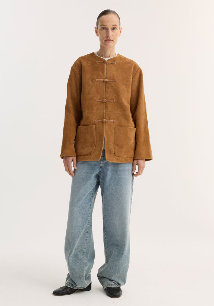 Model in a Pankou closure suede jacket | cognac with pankou knots, patch pockets, light-wash jeans, and black loafers, standing in a catalog pose.