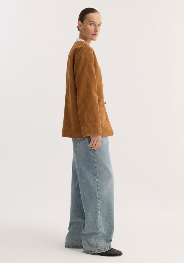 Pankou closure suede jacket in cognac, featuring a side-profile view with embroidered edges, patch pockets, worn over a white top with jeans and slip-on shoes.