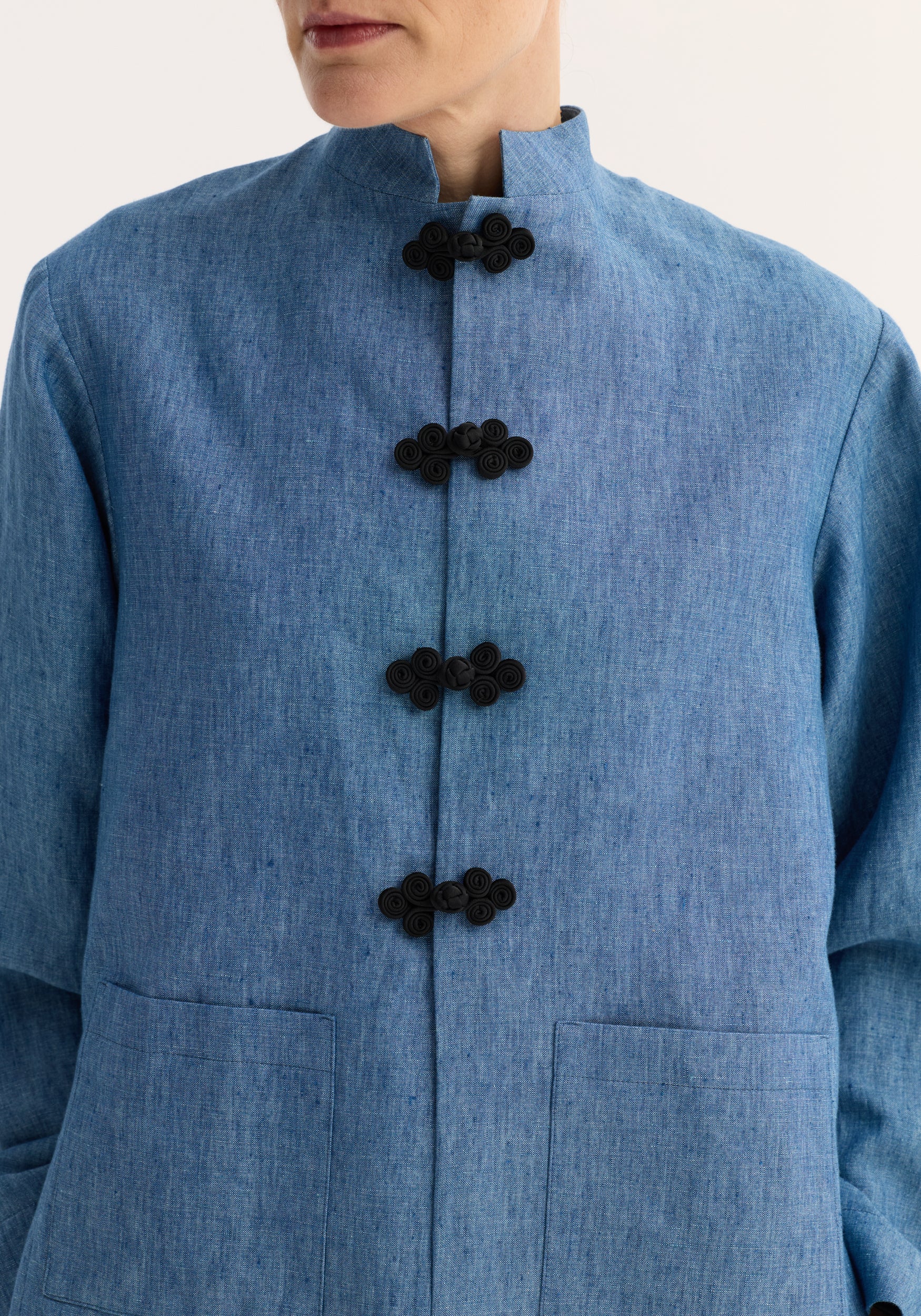 Close-up of a person wearing a pankou closure jacket | ocean blue, featuring a high collar and four traditional black pankou frog closures on a textured blue fabric.