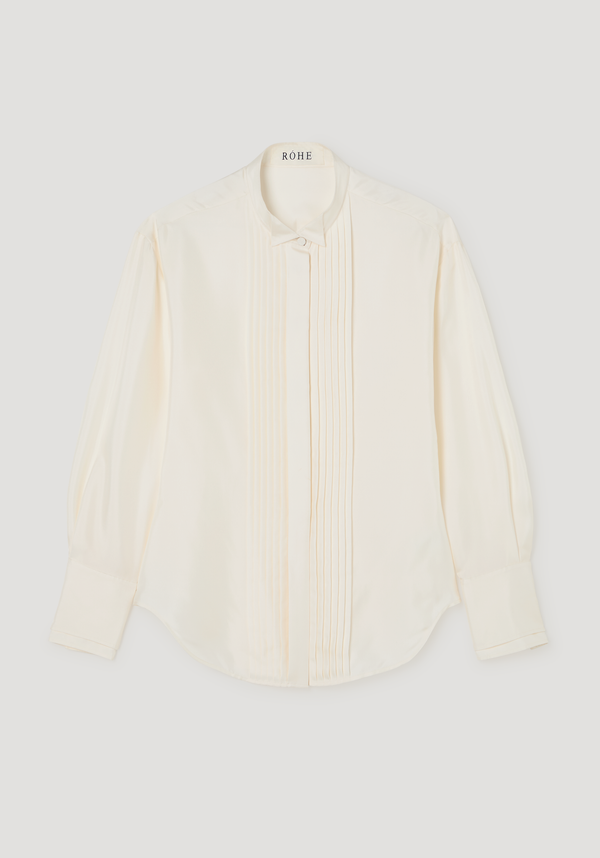 Shaped tuxedo silk shirt | cream featuring a stand-up collar, vertical pintucks, and high cuffs. Crafted from 100% silk, offering a waisted fit and curved hemline.