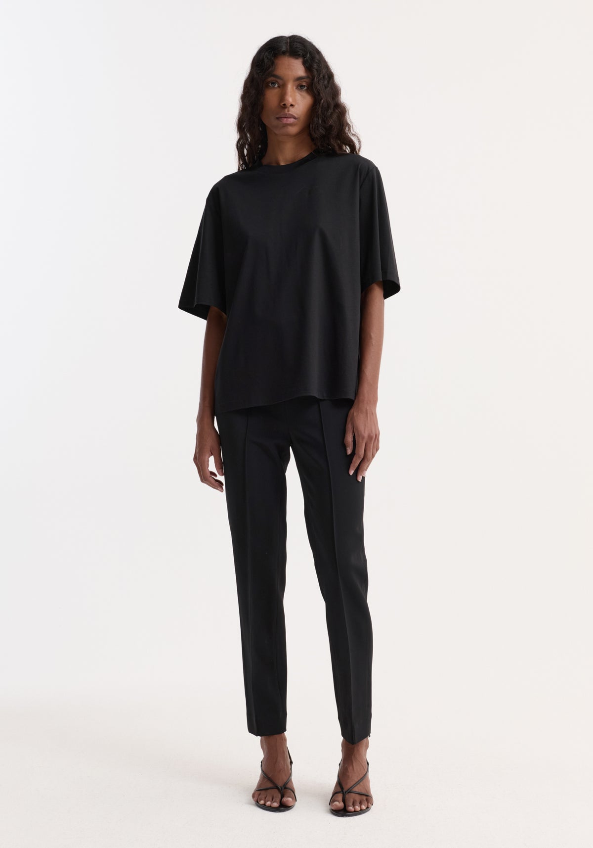 Model wearing Oversized cotton silk t-shirt | black with an oversized fit, paired with black trousers and strappy sandals against a light background