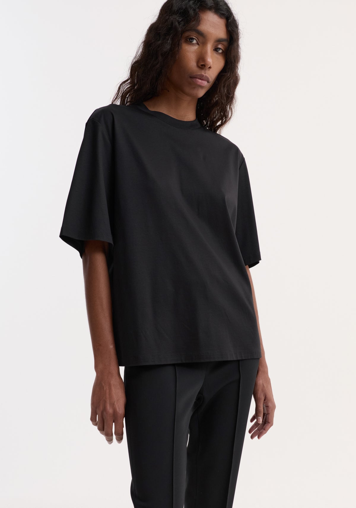 Model wearing Oversized cotton silk t-shirt | black with a relaxed fit, short sleeves, and minimalist styling over black trousers against a neutral background
