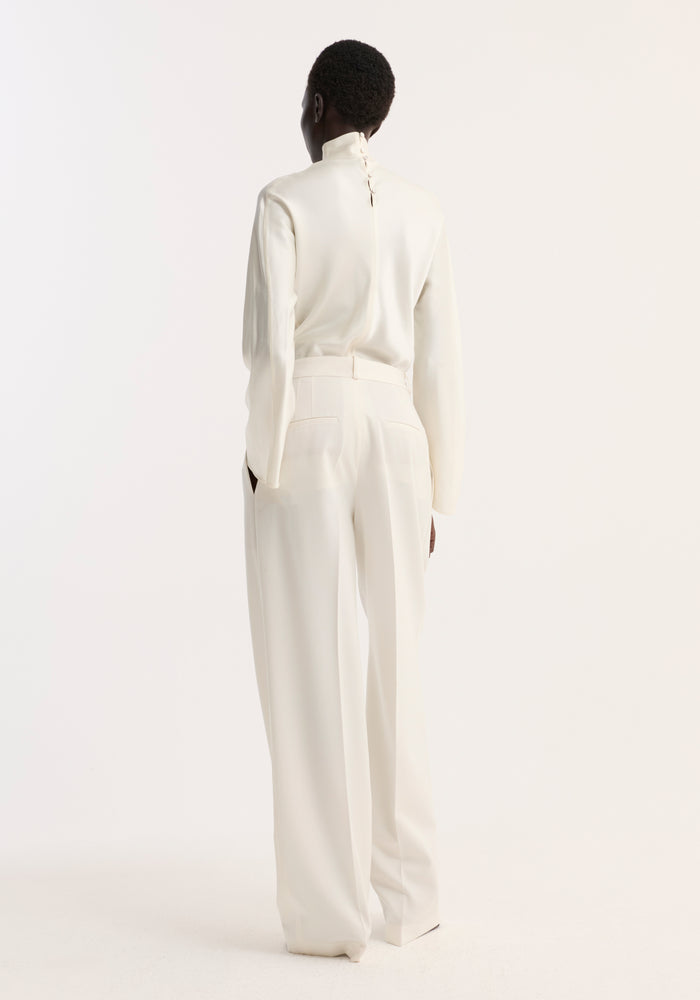 Model wearing Satin waisted top in cream, showcasing a back view with a buttoned high-neck design, paired with wide-leg tailored trousers.