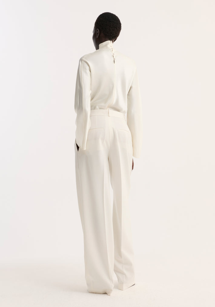 Model wearing Satin waisted top in cream, showcasing a back view with a buttoned high-neck design, paired with wide-leg tailored trousers.