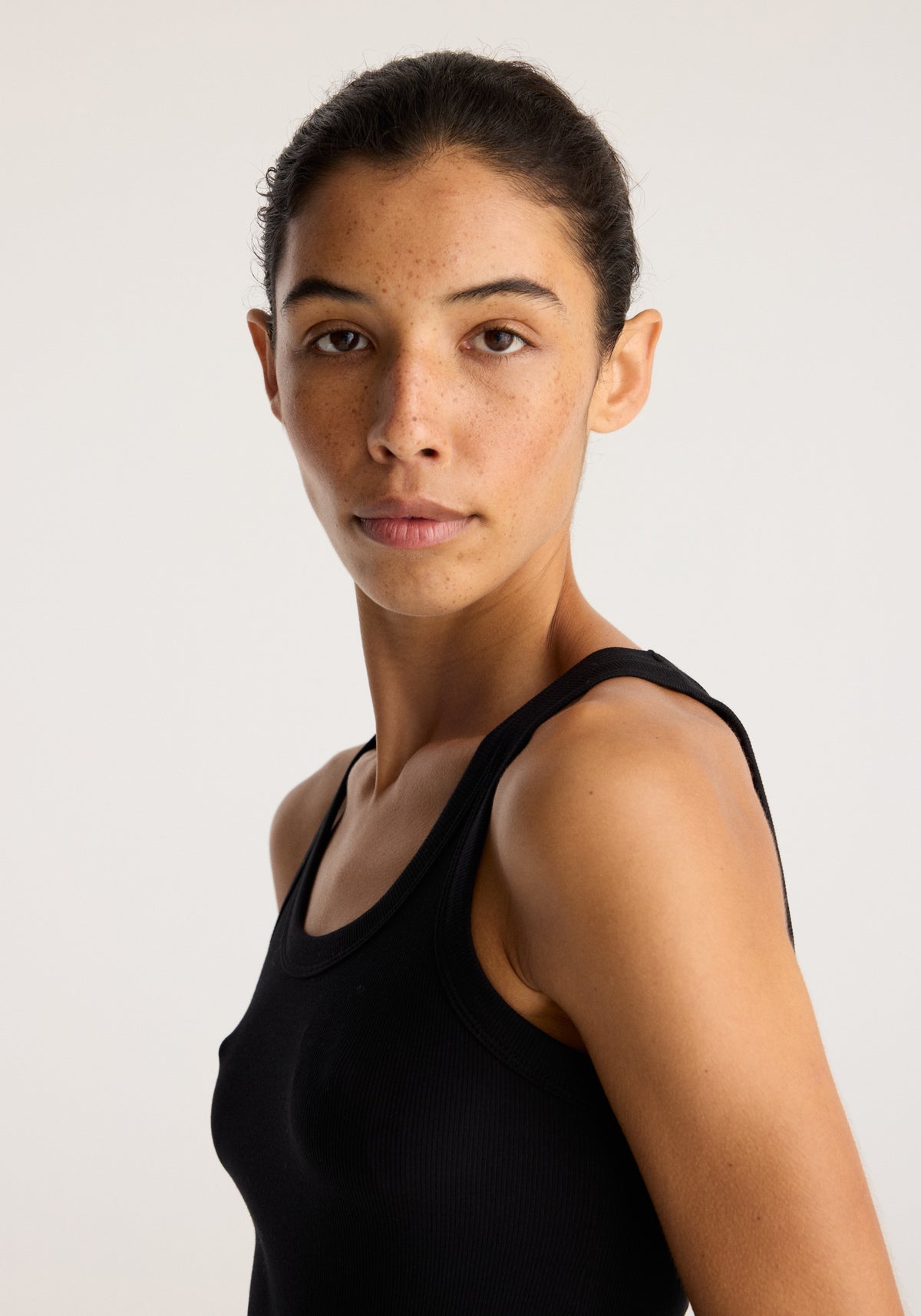 Merino scoop neck top | black worn by a model in a close portrait showing the sleeveless design and scoop neckline
