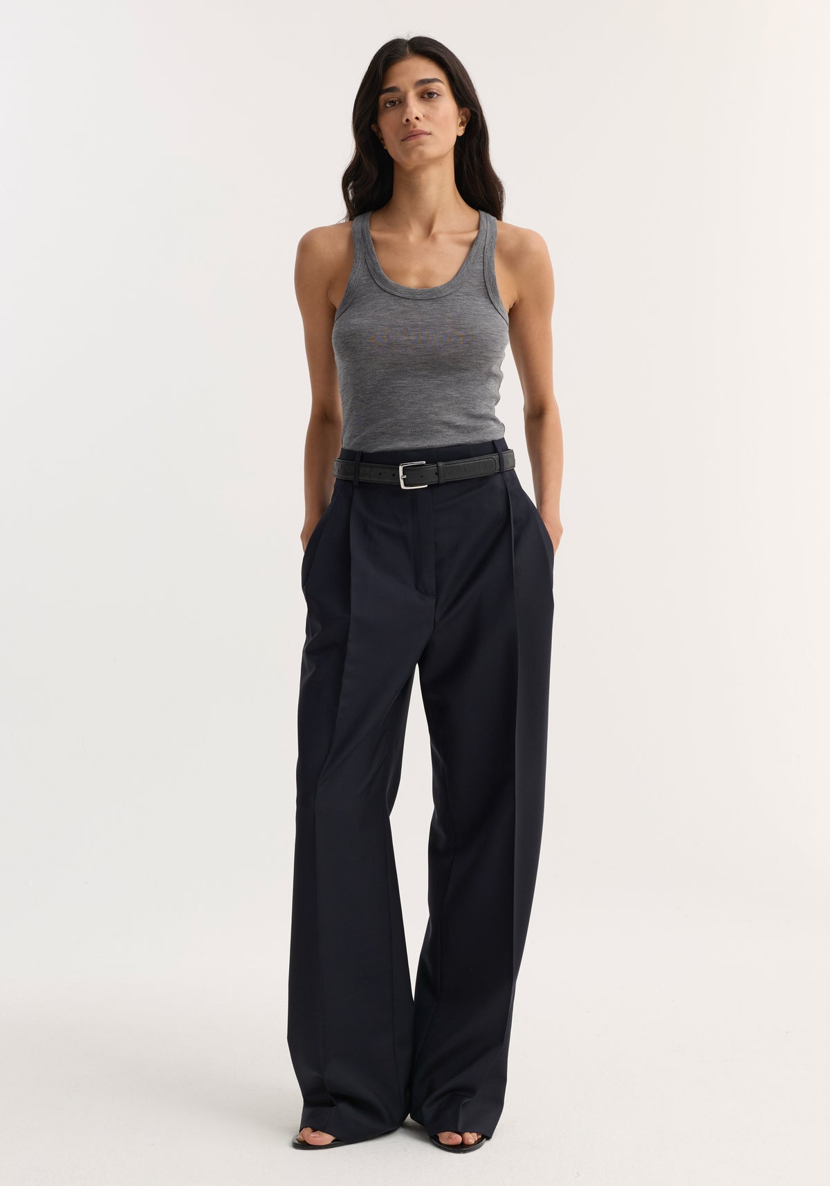 Woman wearing a fitted Merino scoop neck top | mid grey melange paired with high-waisted wide-leg black trousers and a black belt, standing against a plain background.
