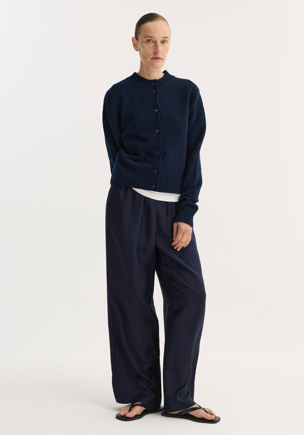 Model wearing Short boiled cardigan | navy, featuring a high crew neck and drop shoulders, paired with wide-leg trousers and black thong sandals.
