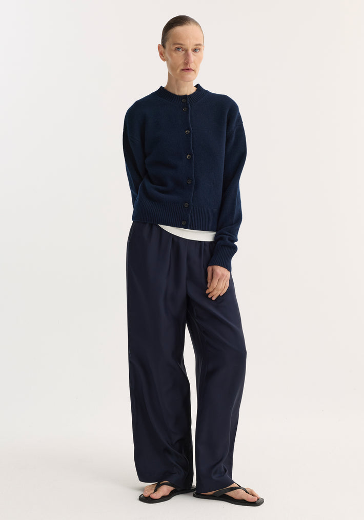 Model wearing Short boiled cardigan | navy, featuring a high crew neck and drop shoulders, paired with wide-leg trousers and black thong sandals.