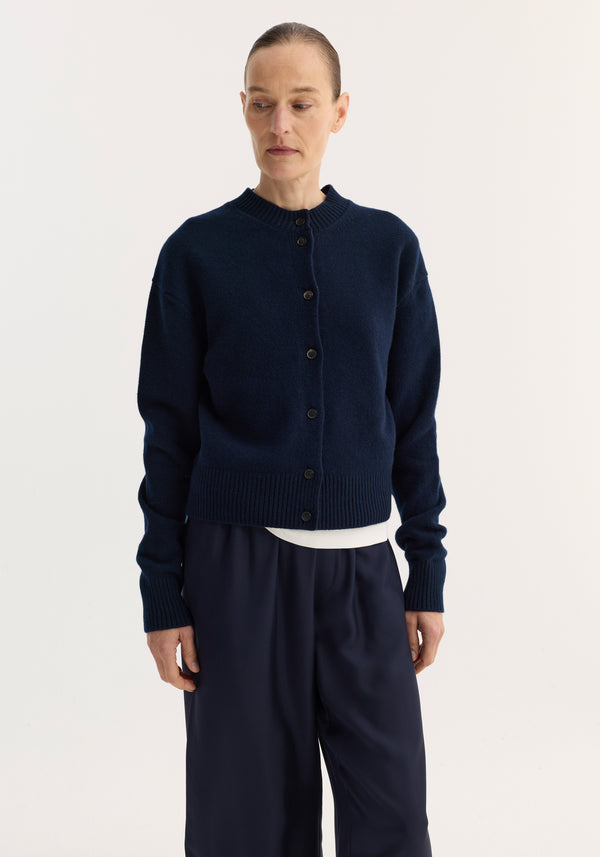 Model wears the Short boiled cardigan | navy, featuring a button-front, ribbed crew neck, drop shoulders, and loose-fit wide-leg trousers against a light backdrop.