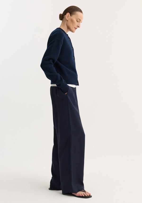 Person models a Short boiled cardigan | navy, showcasing its high crew neck, drop shoulders, and cropped fit, layered over a white T-shirt.