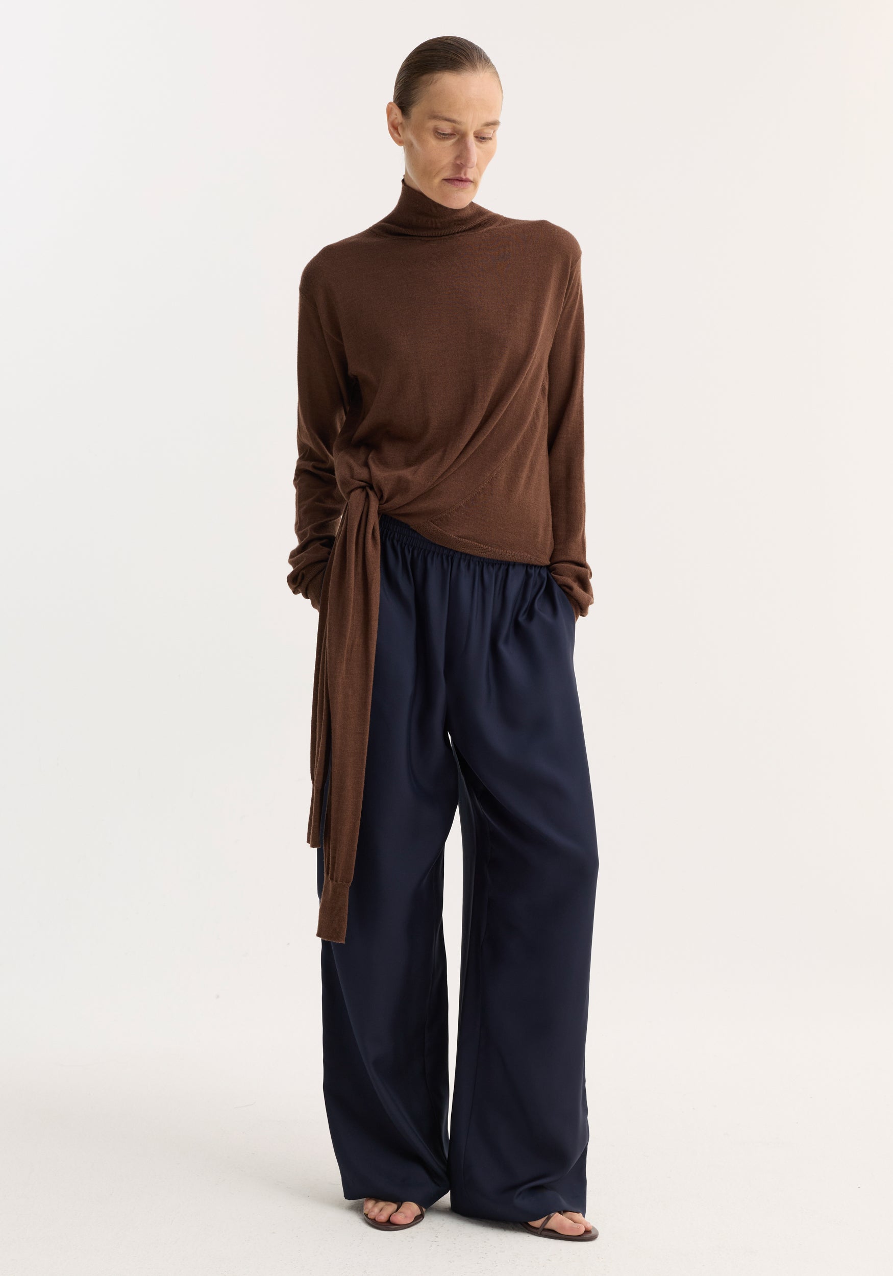 Model wearing Wide leg silk trousers | night, showcasing relaxed drape and fluidity with elasticated waistband and drawstring, paired with a knotted turtleneck sweater.