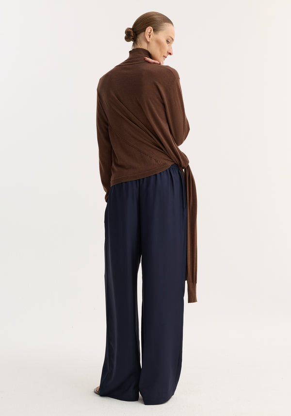 Wide leg silk trousers | night, shown from behind, showcasing their relaxed drape, elasticated waistband, and drawstring, worn by a person with hair in a low bun.