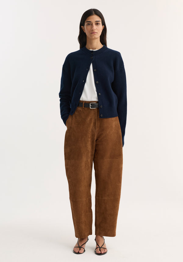Model wearing Sculptural suede trousers | tobacco with panel seams, paired with a navy cardigan and strappy sandals, showcasing a modern, minimalist autumn look.