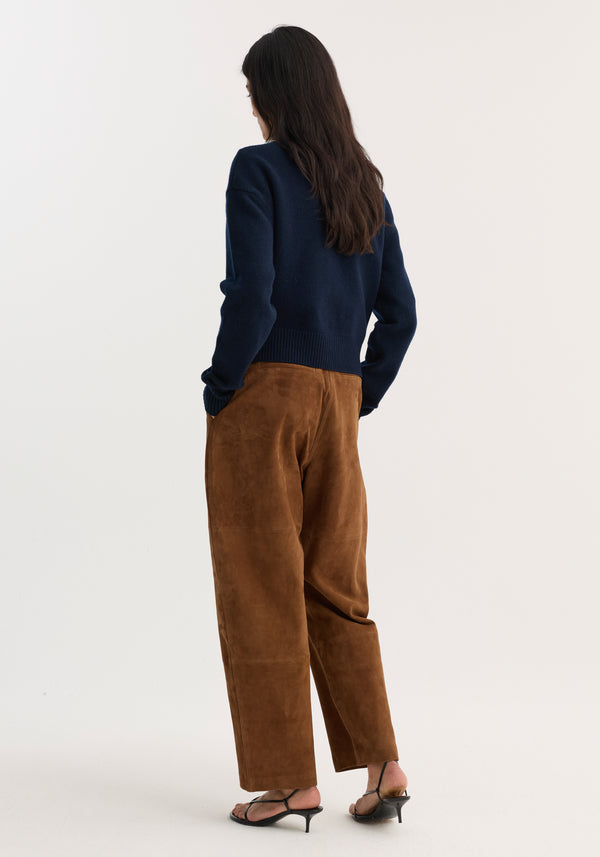 A person wears Sculptural suede trousers | tobacco, showcasing wide barrel legs, panel seam detailing, and back pockets, paired with black slingback sandals.