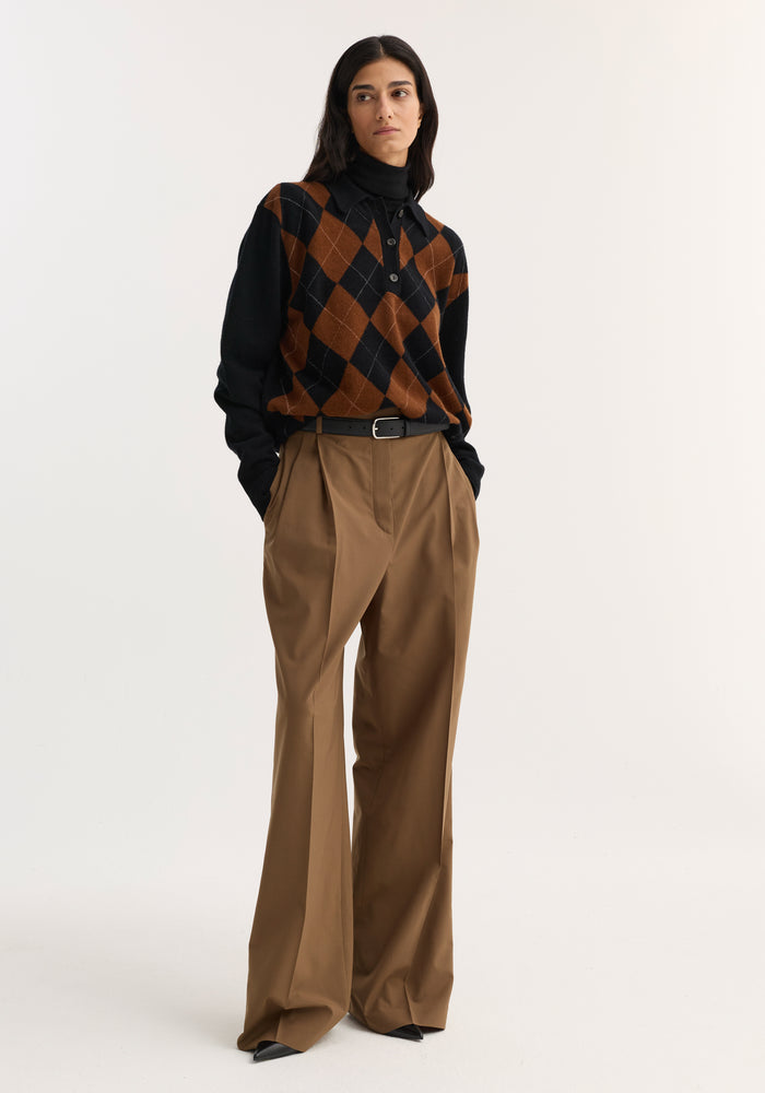 Model wearing Mid-waist tailored trousers in mocha with a wide leg, double pleats, and a structured waistband, styled with a black turtleneck and argyle sweater.