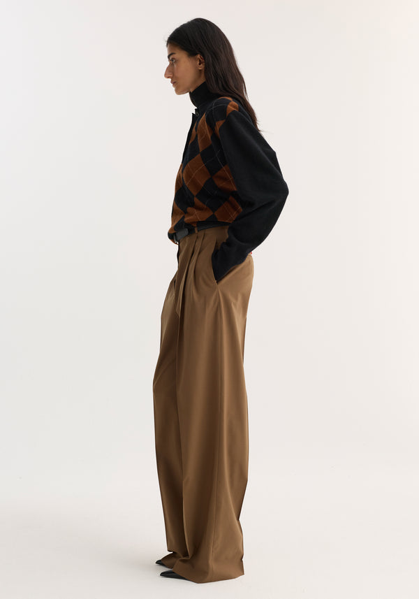 Woman models Mid-waist tailored trousers in mocha, featuring a structured waistband, double pleats, and wide legs, styled over black pointed-toe shoes.