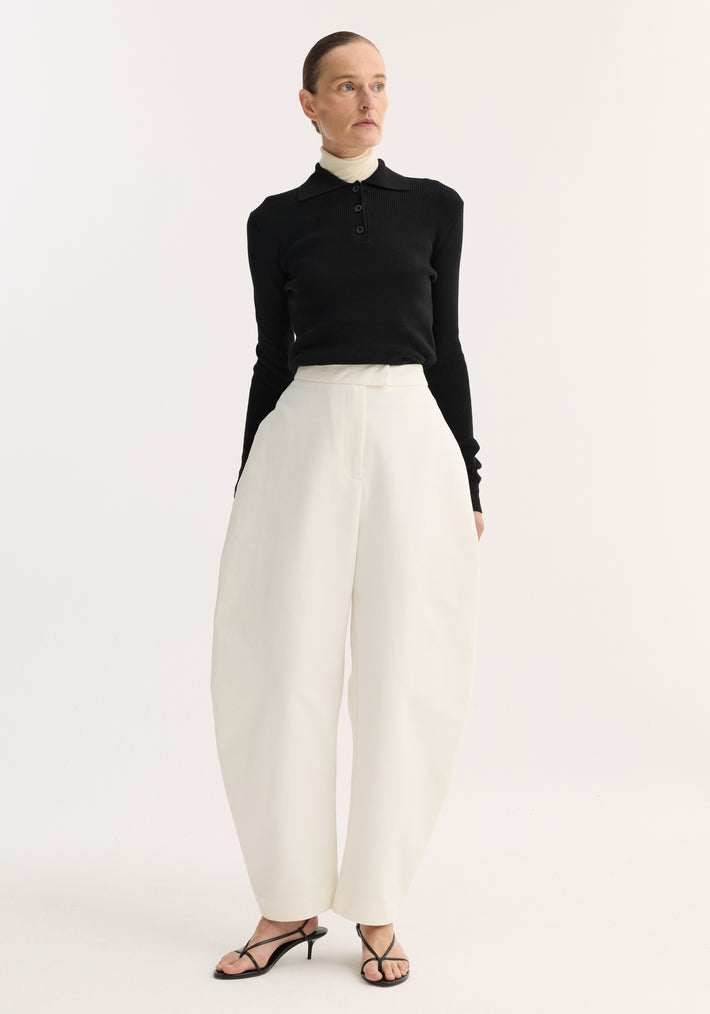 Model wearing sculptural trousers | paper white, featuring a high waist and balloon leg. Paired with a layered knit top and strappy heeled sandals.