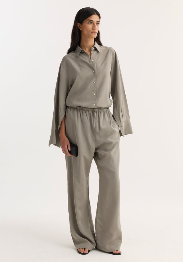 Woman wearing Relaxed fit trousers | light grey stripe, featuring a drawstring waistband and wide leg, styled with a matching shirt and black sandals.